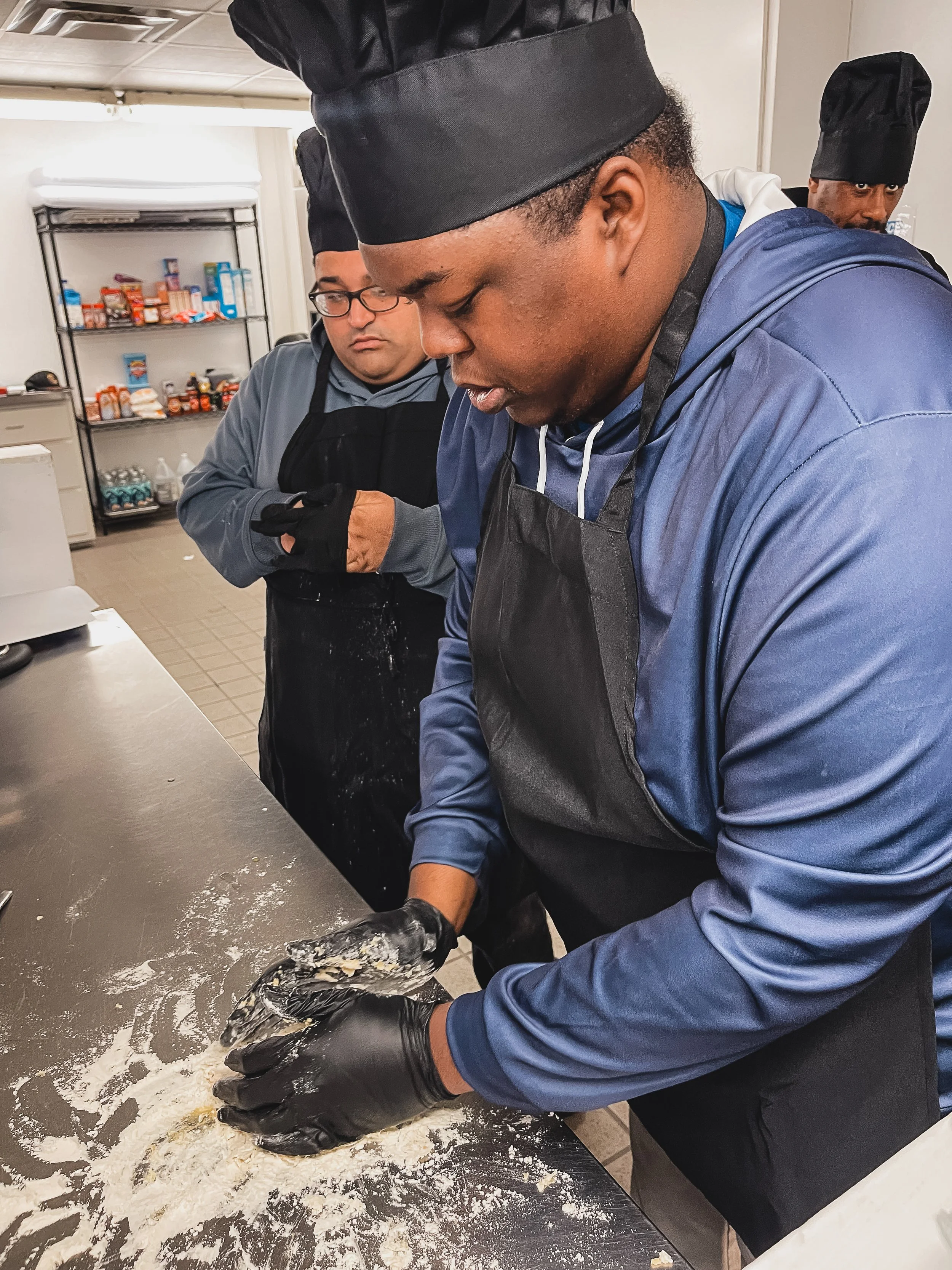 Image shows participant learning to make pizza dough in a professional kitchen
