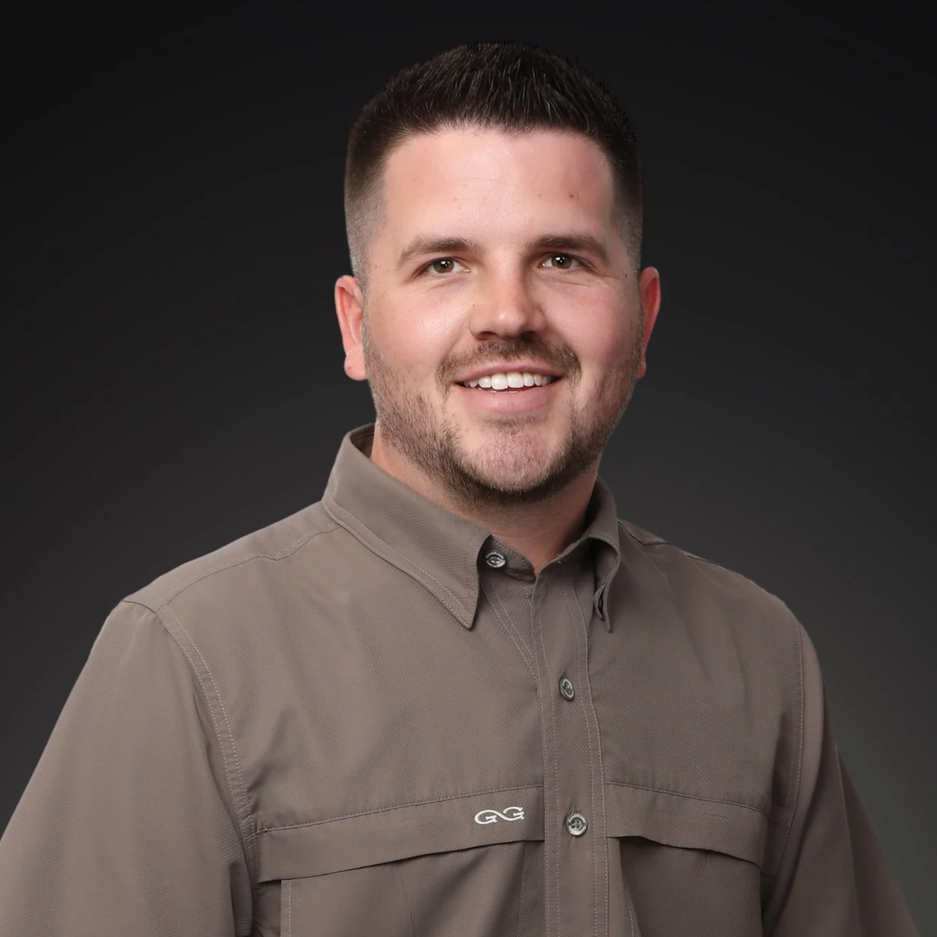 A smiling man with short dark hair standing in front of a dark gradient background I Scott Brown Properties I Denton, TX