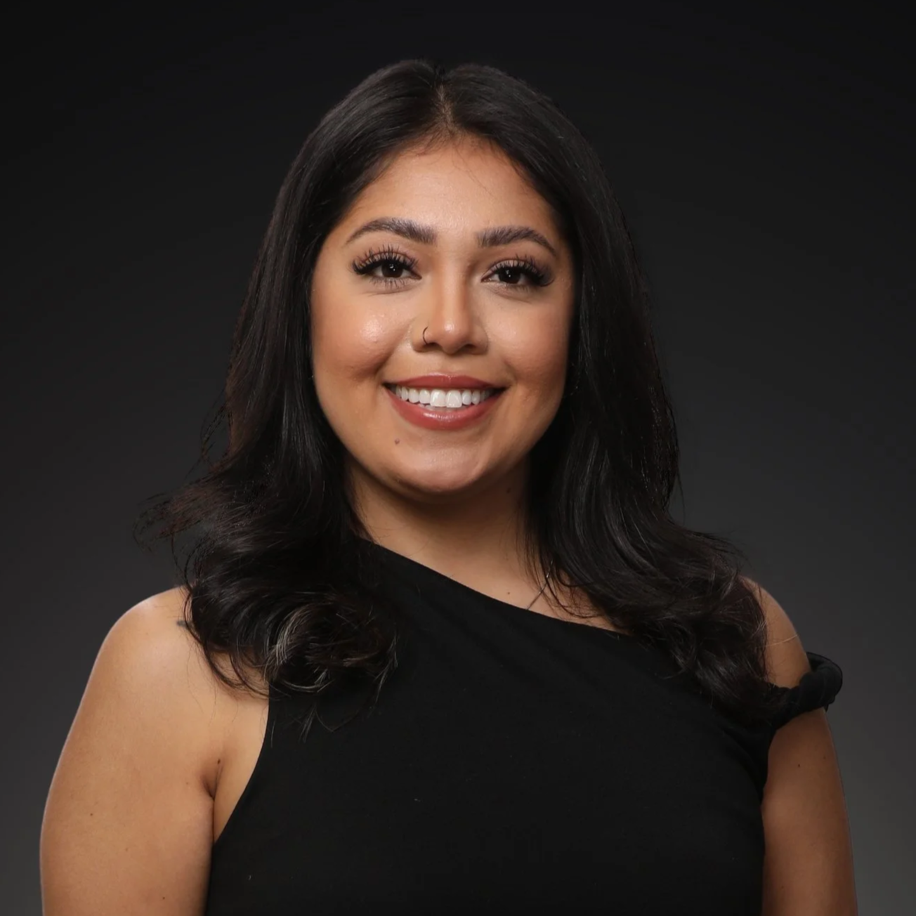 A smiling woman with long, wavy dark hair and pearl earrings, wearing a black and white floral blouse I Scott Brown Properties I Denton, TX