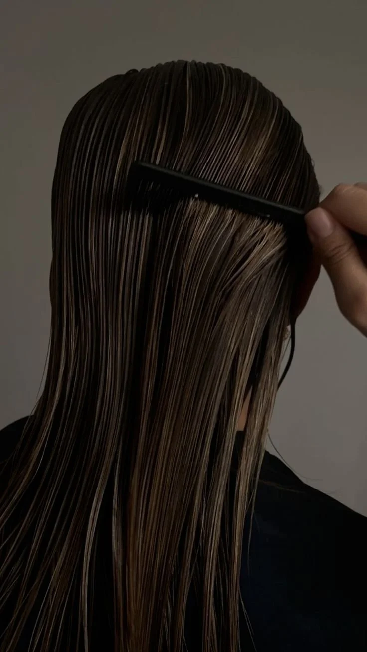 A person having their hair straightened with a wide-tooth comb, with wet, light brown hair draped over their shoulder.