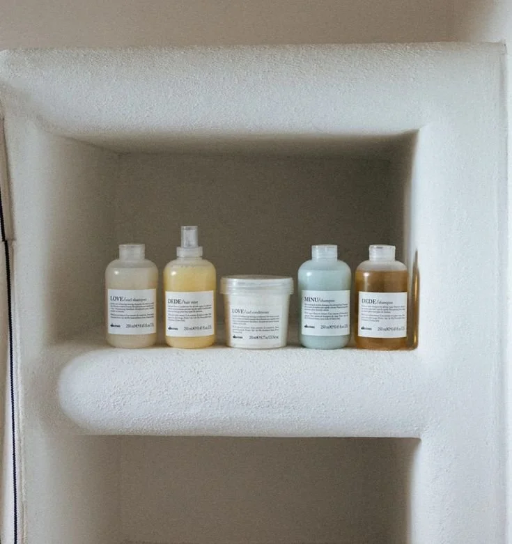 Collection of five shampoo and hair care bottles on a white shelf in a bathroom.