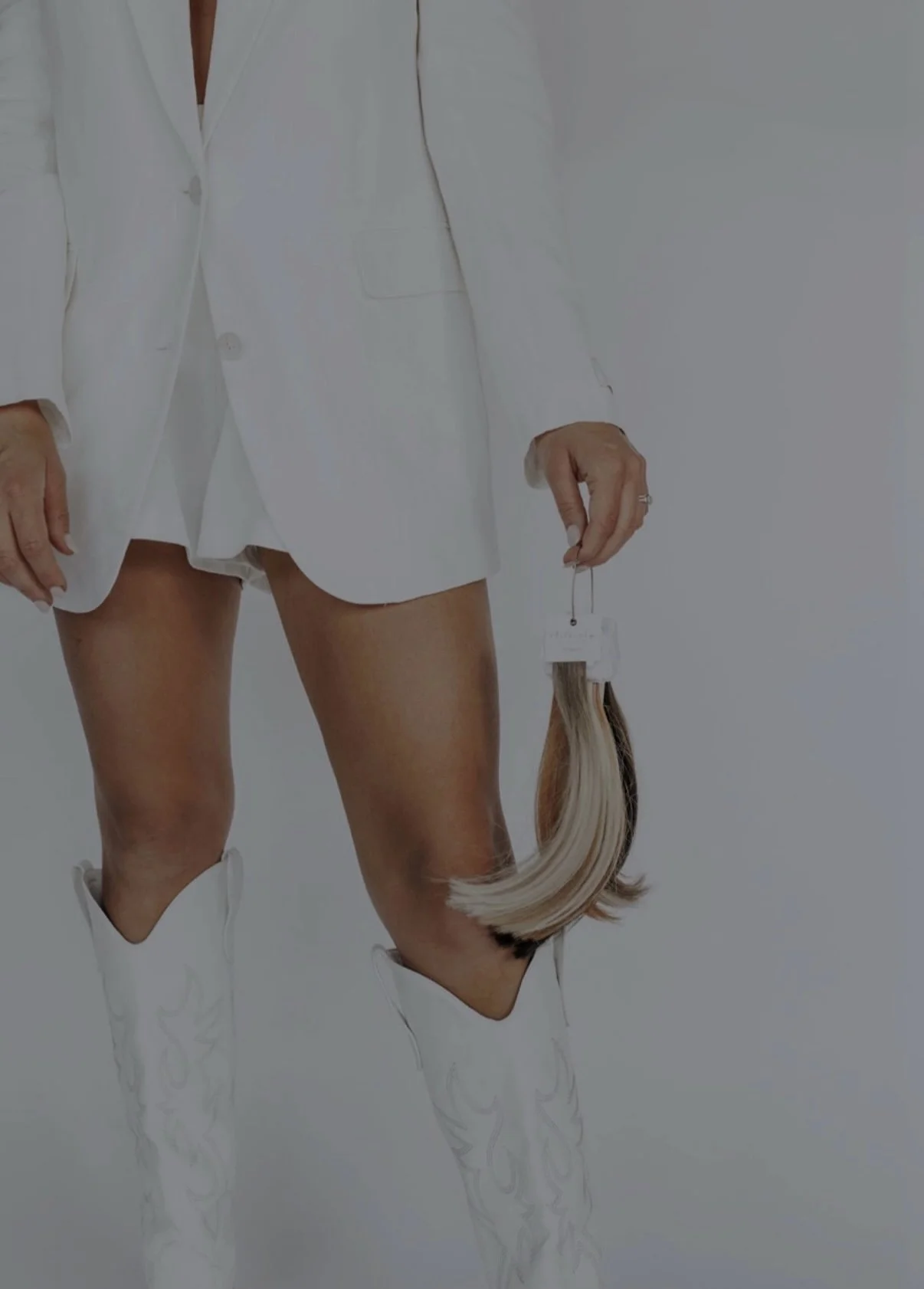 Person wearing a white blazer and thigh-high white boots, holding a hair piece.