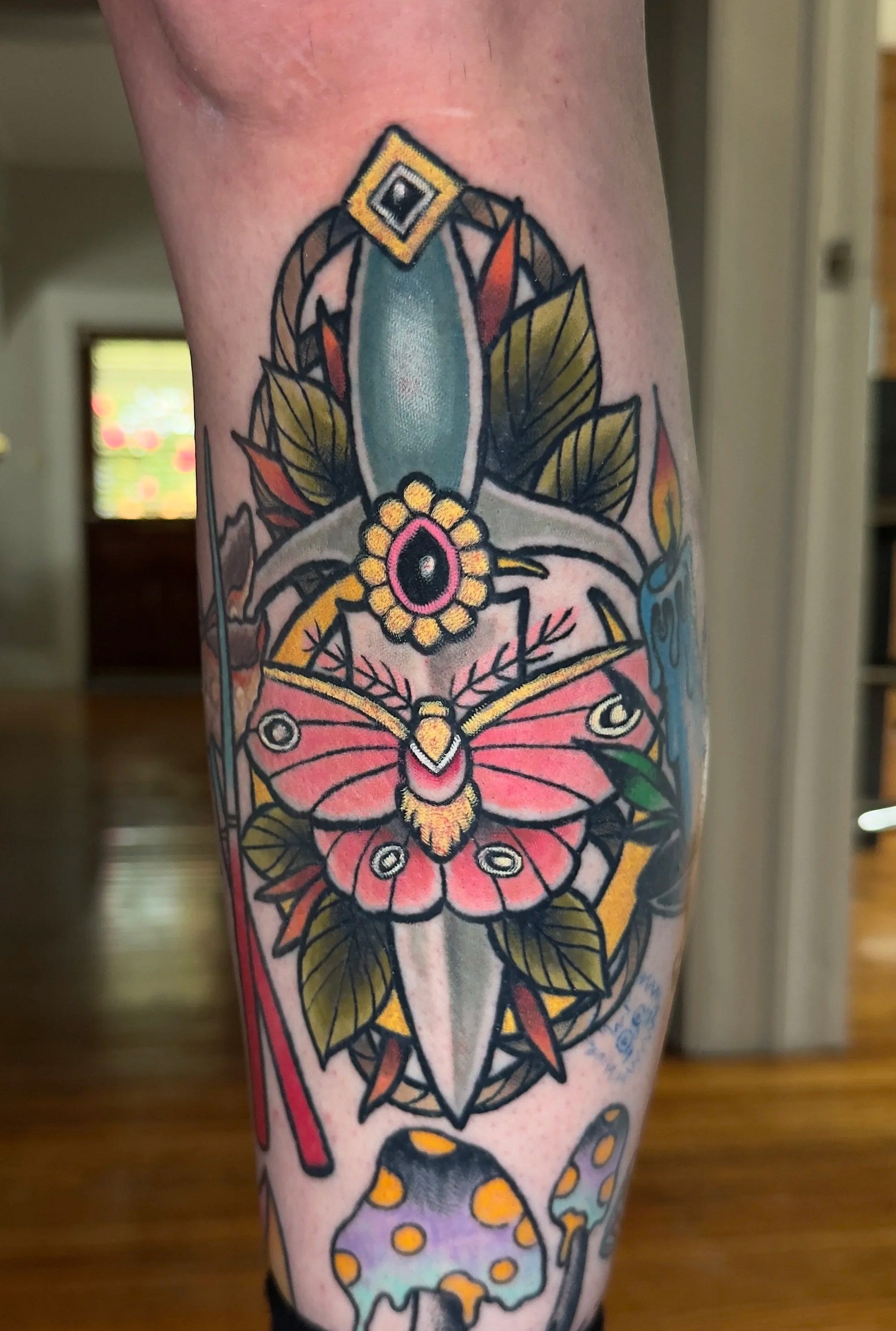 Colorful tattoo of a butterfly and mushrooms on a person's calf, with leaves and abstract shapes.