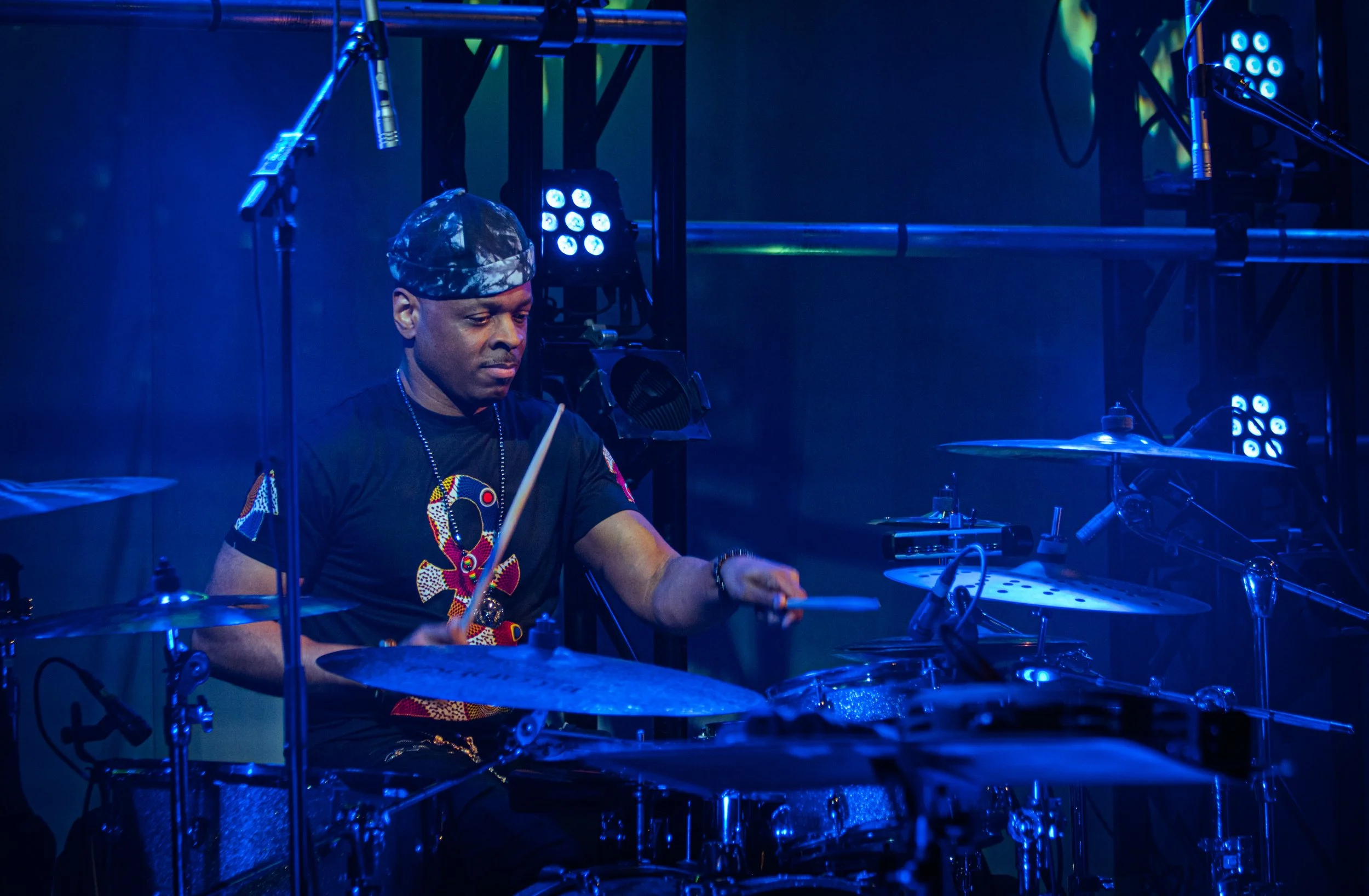 A man playing drums on a stage with blue and green lights.