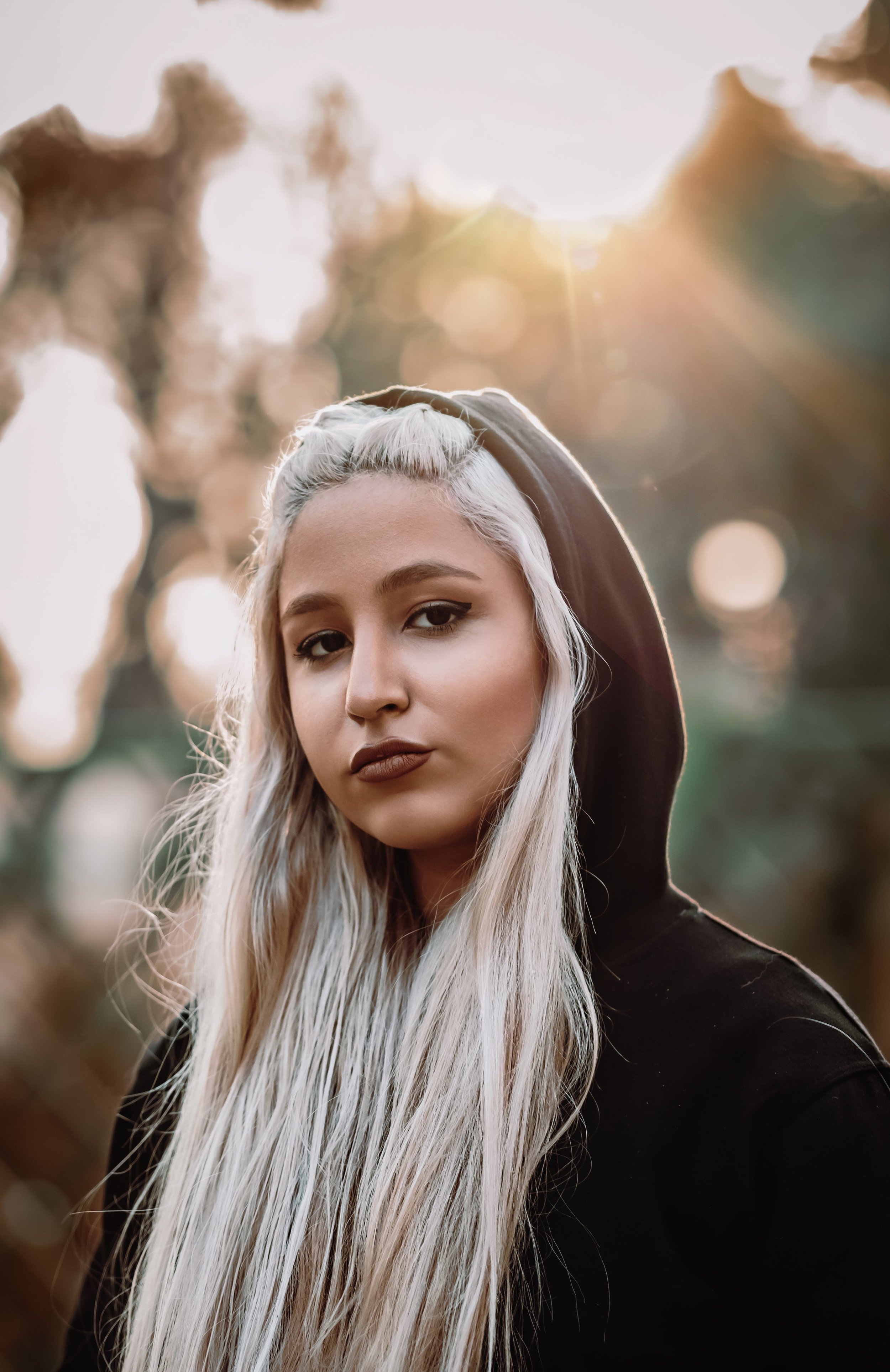 Woman with long blonde hair wearing a black hoodie, sunlight in background
