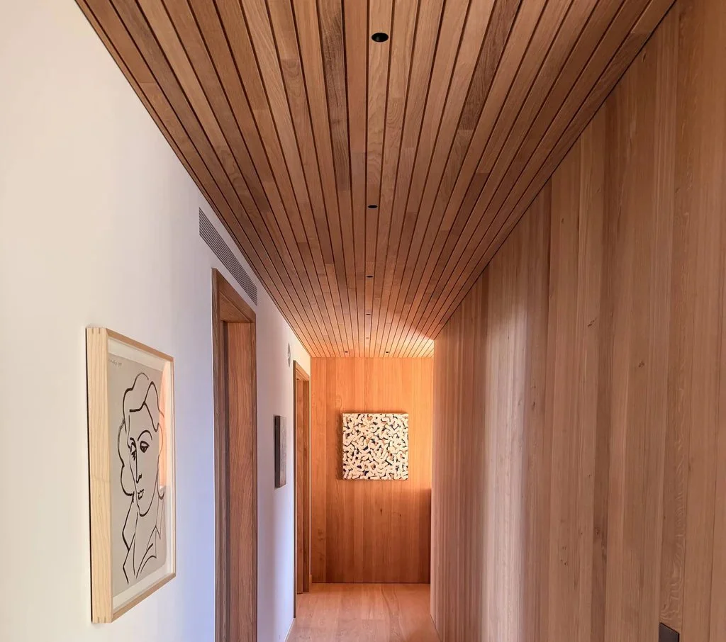 A hallway with a wooden ceiling and walls, featuring minimalist artwork on the walls.
