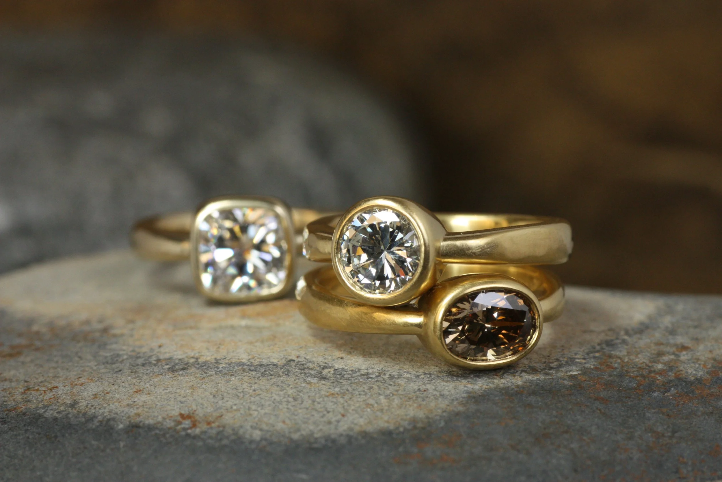 three diamond bezel engagement rings arranged together on a rock