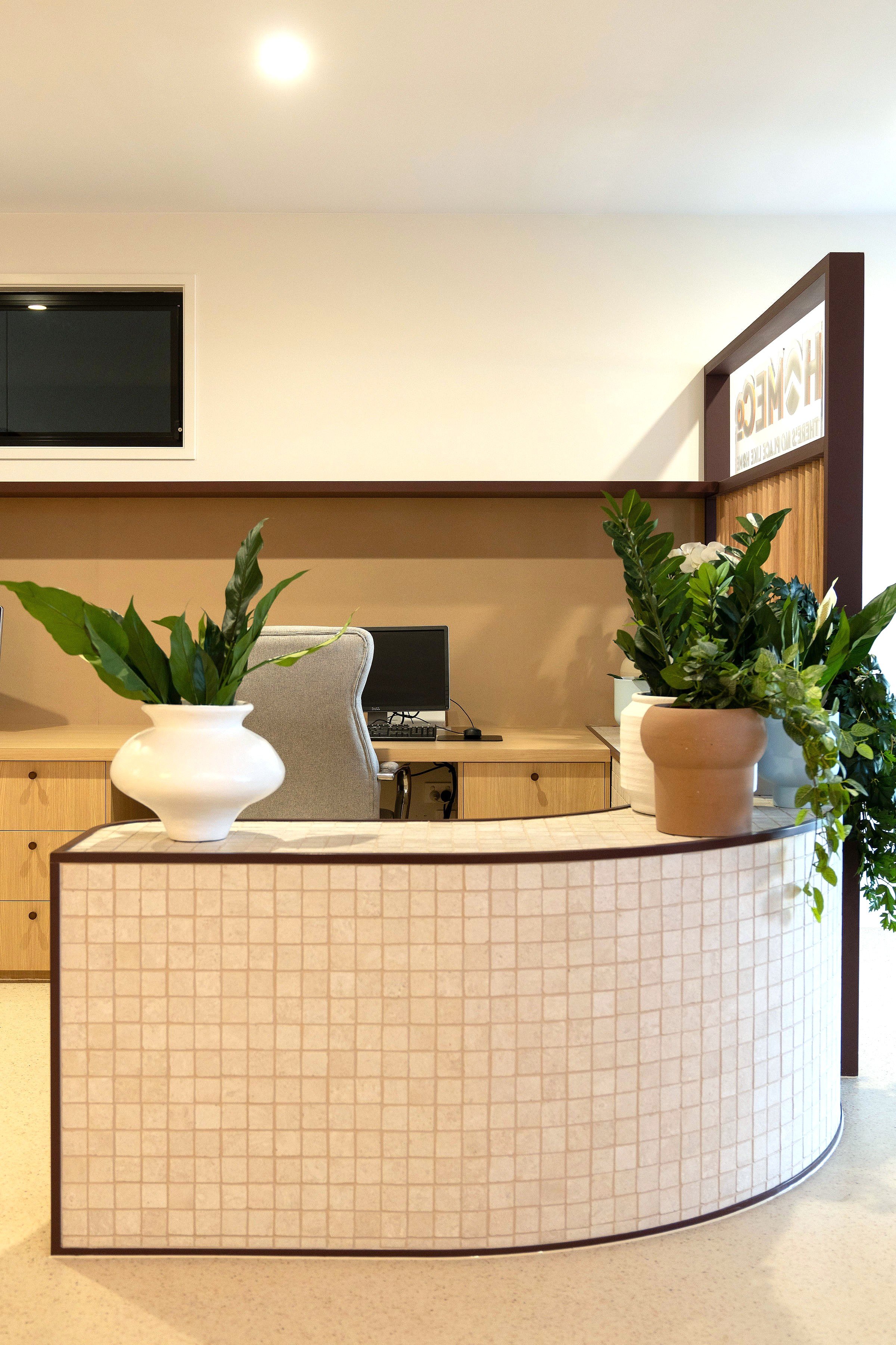 Reception area with a curved counter, potted green plants, and a computer behind the counter.