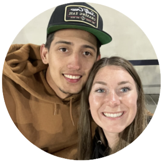 Photo of Amber & Neven- White man smiles in a brown hoodie and a green baseball cap, while white woman with long brown hair smiles next to him in front of a white background.