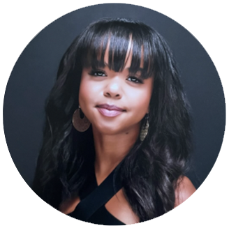 Photo of Ivy Angst- brown woman with long black hair and bangs smiles in front of a black background