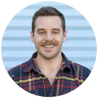 Photo of Travis Althouse: white man with short brown hair wearing red plaid button down shirt standing against a blue wall