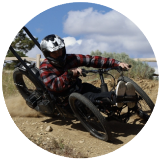 Photo of Caleb- White man wears a motorcycle helmet on a bike in the dirt outside.