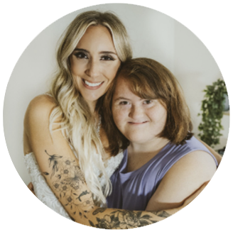 Photo of Sarah & Emily- 2 white white smile and hug each other. One has long blonde hair, the other has short red hair.