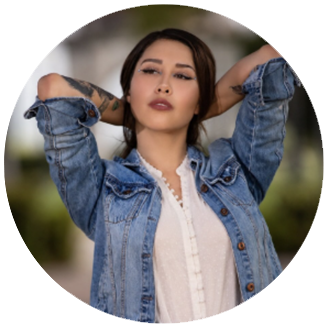 Photo of Vanessa- woman with a white shirt and a jean jacket on stars into the distance with her hands touching the back of her head