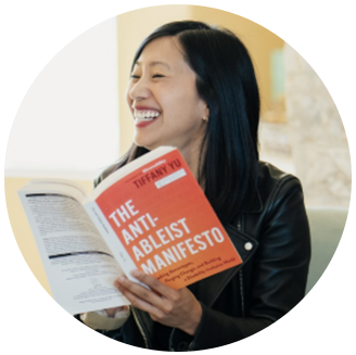 Photo of Tiffany Yu- Asian woman with long dark hair smiling while holding the book "the anti-ableist manifesto" that she wrote