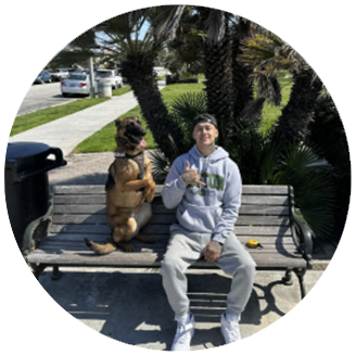 Photo of white man and large dog sitting on a park bench smiling.