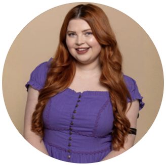 Photo of Jenni- white woman with long wavy red hair smiles in a purple shirt in front of a light brown backdrop