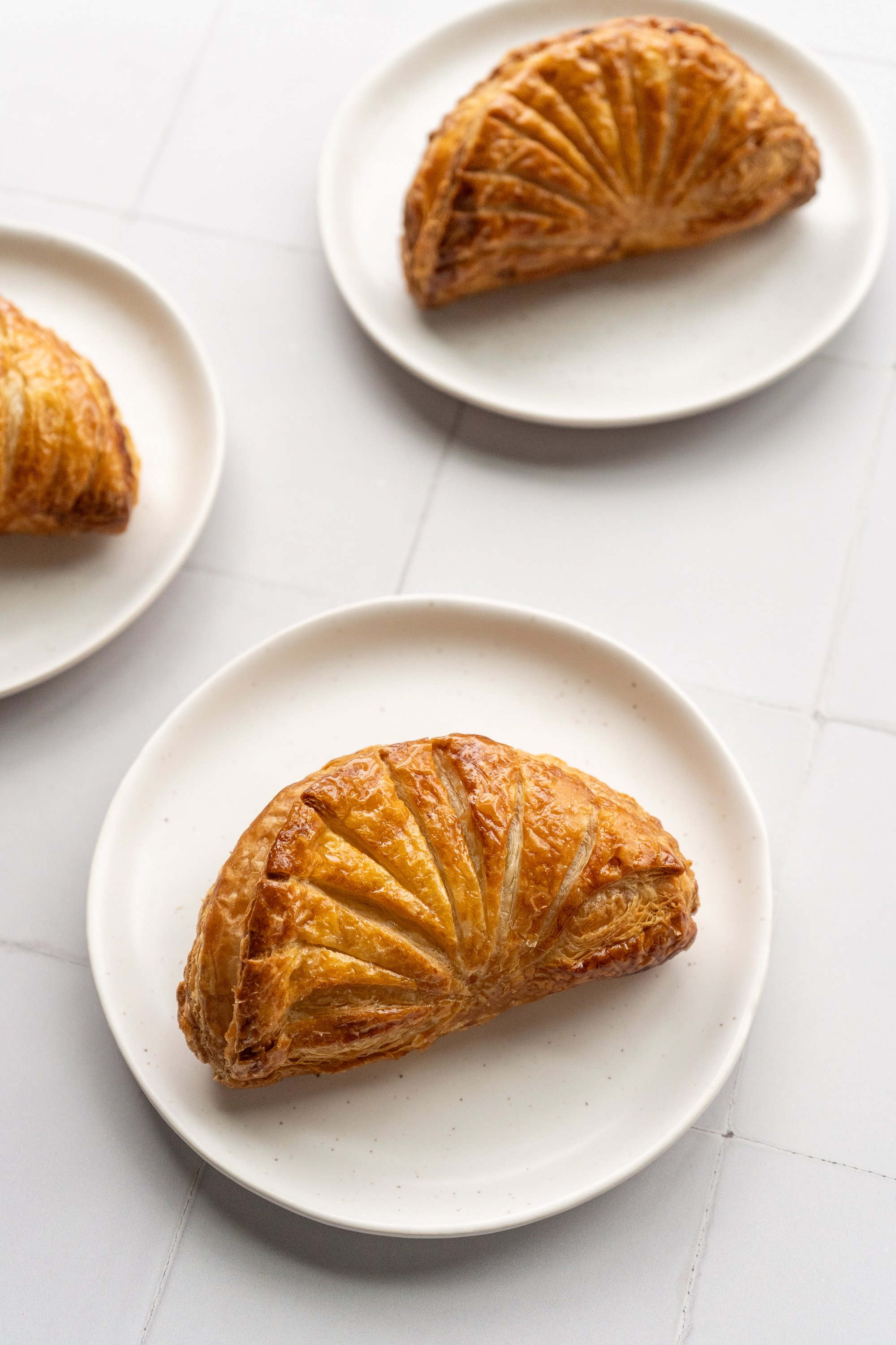 Three plates with baked croissants on a white surface.