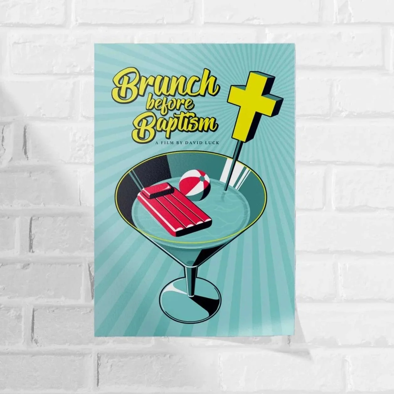 Poster promoting a film titled 'Brunch before Baptism' shows a martini glass filled with water, containing a red things that looks like a pool float, a beach ball, and a yellow cross on a stick.