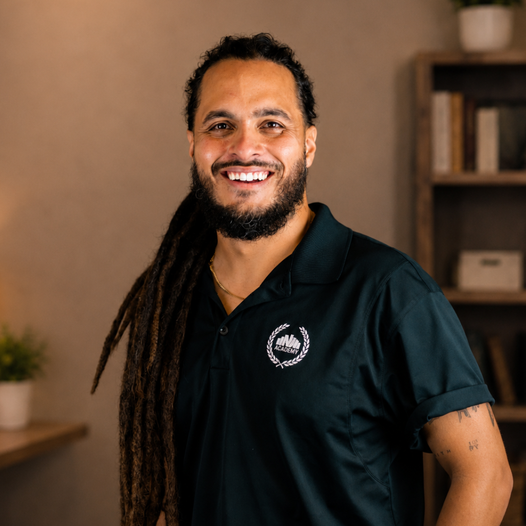 A man with long dreadlocks, beard, and mustache smiling in front of a brick wall, wearing a green Teenage Mutant Ninja Turtles T-shirt.