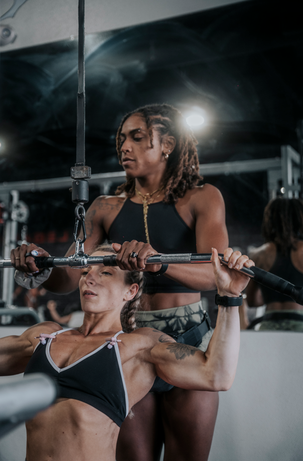 A woman performing a bench press exercise with a barbell while a trainer spots her in a gym.