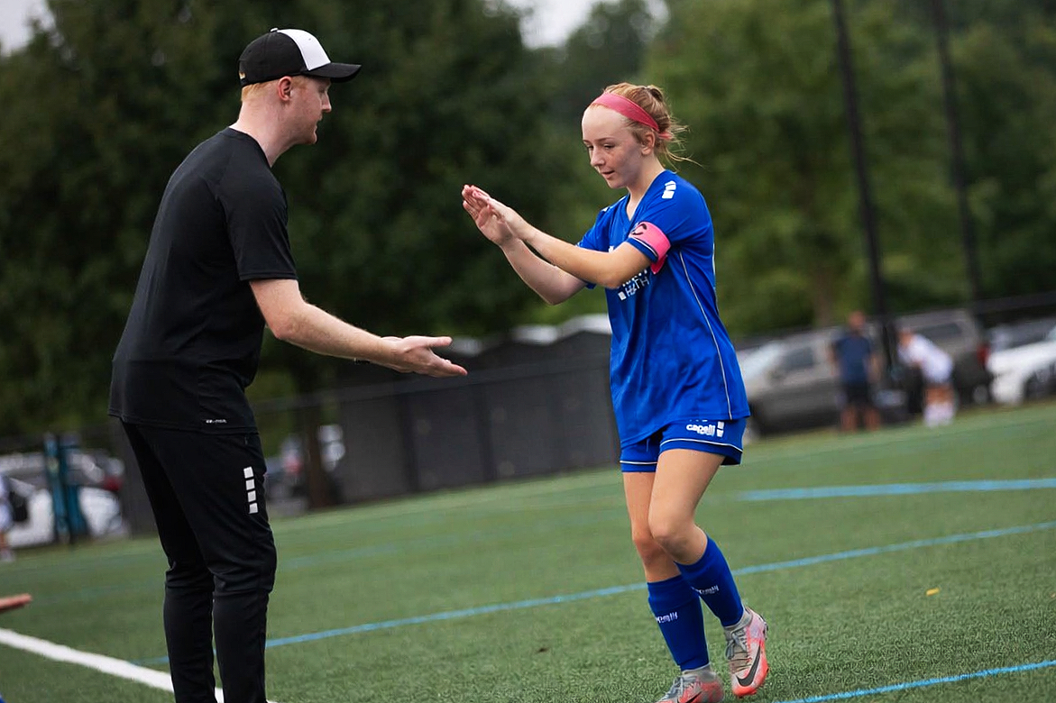 A coach high fiving his female soccer player coming off of the field