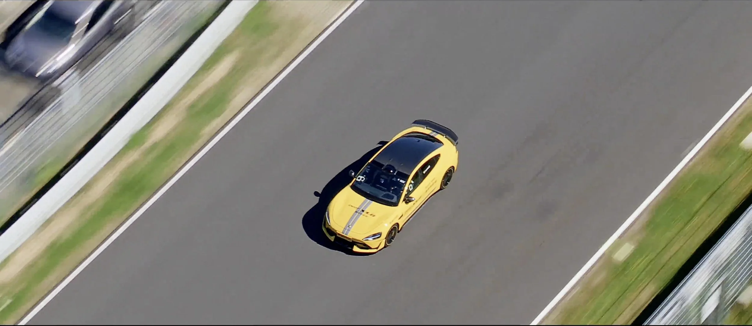 A yellow sports car with black racing stripes is driving on a race track.