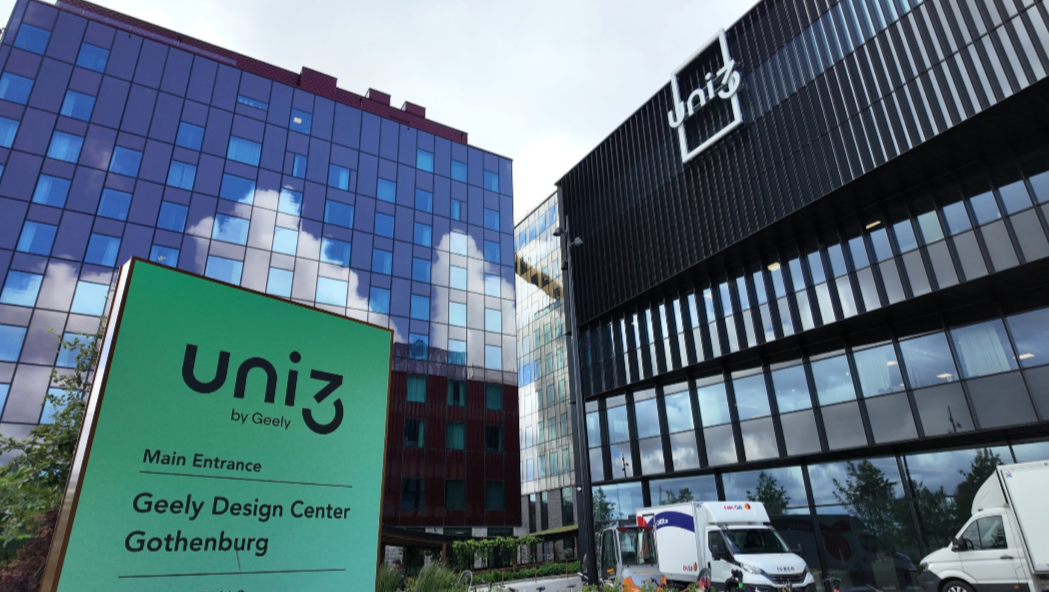 Modern office buildings with glass facades, one with the 'uniz by Geely' logo, and an informational sign for the Geely Design Center in Gothenburg, Sweden, visible in the foreground.