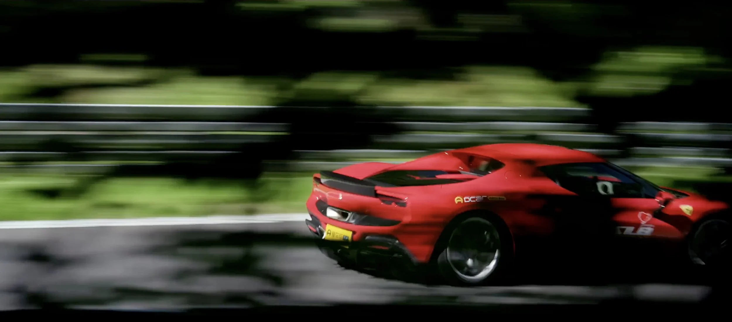 Red sports car speeding on a race track with a blurred background of green trees and fencing.