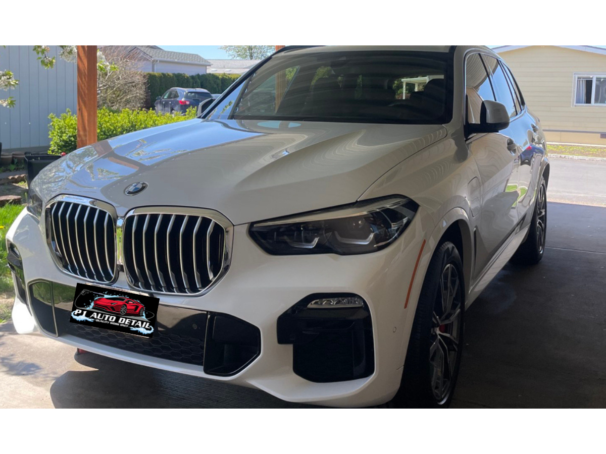 White BMW SUV parked in a garage with a car dealership license plate frame reading P1 Auto Detail.