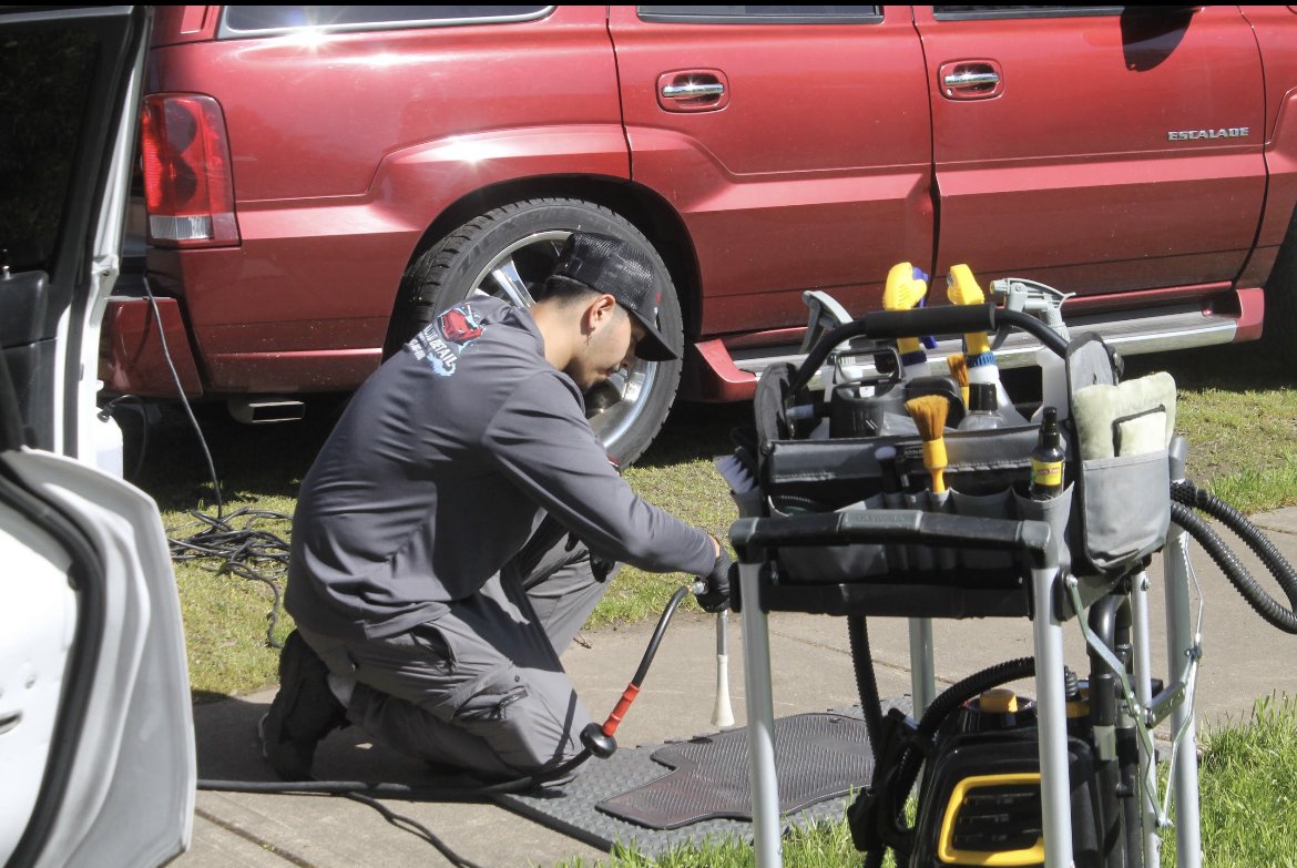 A technician kneeling on the sidewalk working with equipment in front of a red Escalade SUV.