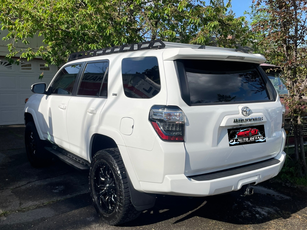 White Toyota 4Runner SUV parked outdoors near trees and a garage.