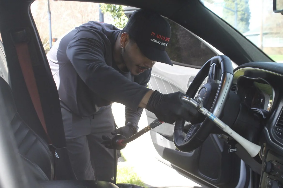 A mechanic working on the interior of a truck, using a blow torch near the steering wheel inside the vehicle.