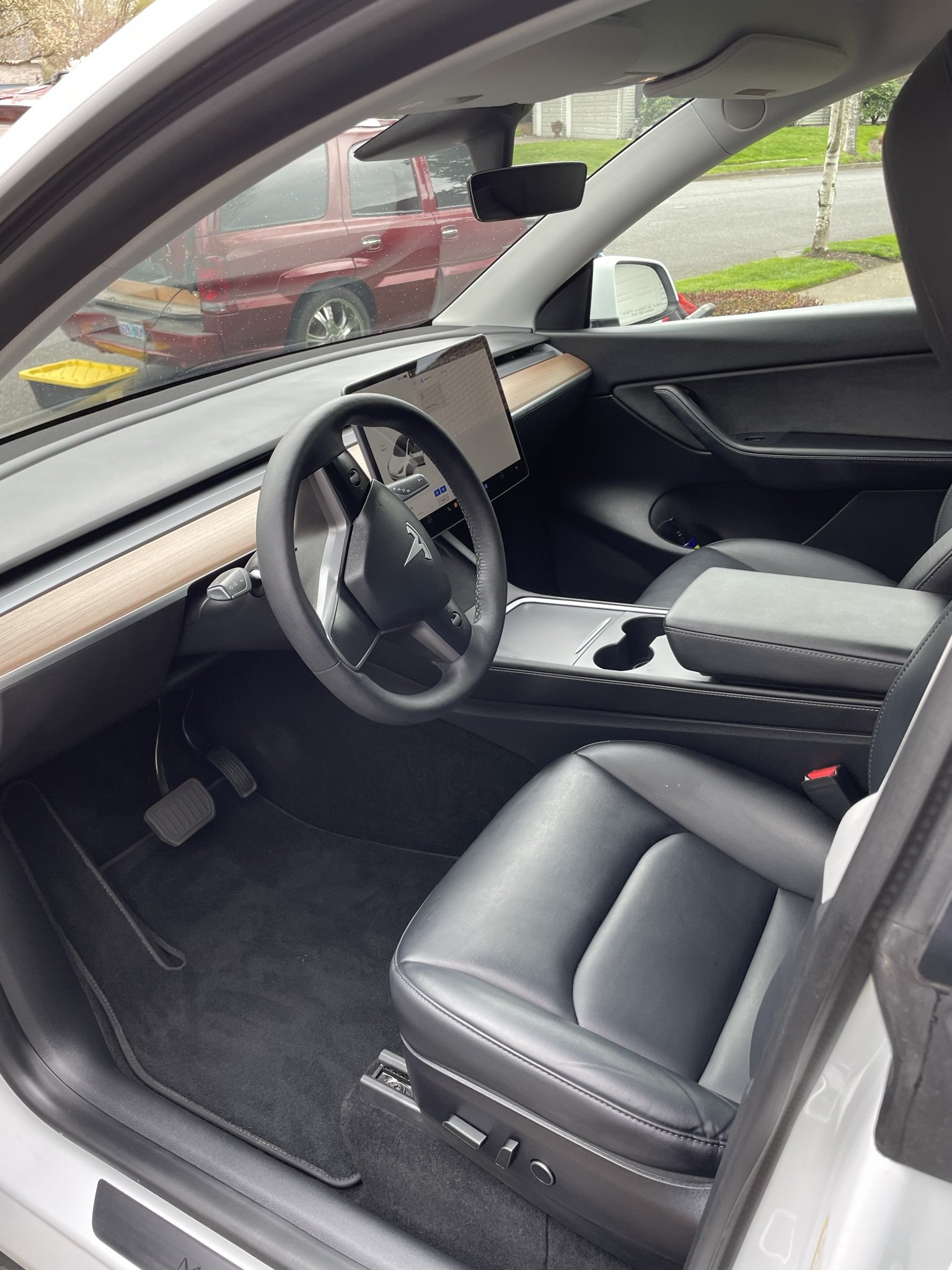 Interior of a Tesla vehicle showing a steering wheel, dashboard with a large touchscreen display, black leather seats, and a center console.