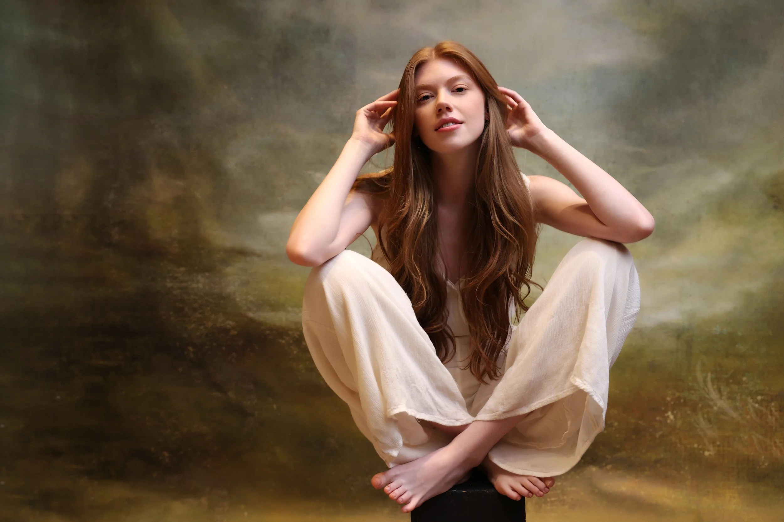 Female senior with red hair sitting cross-legged in a light, ethereal studio setting