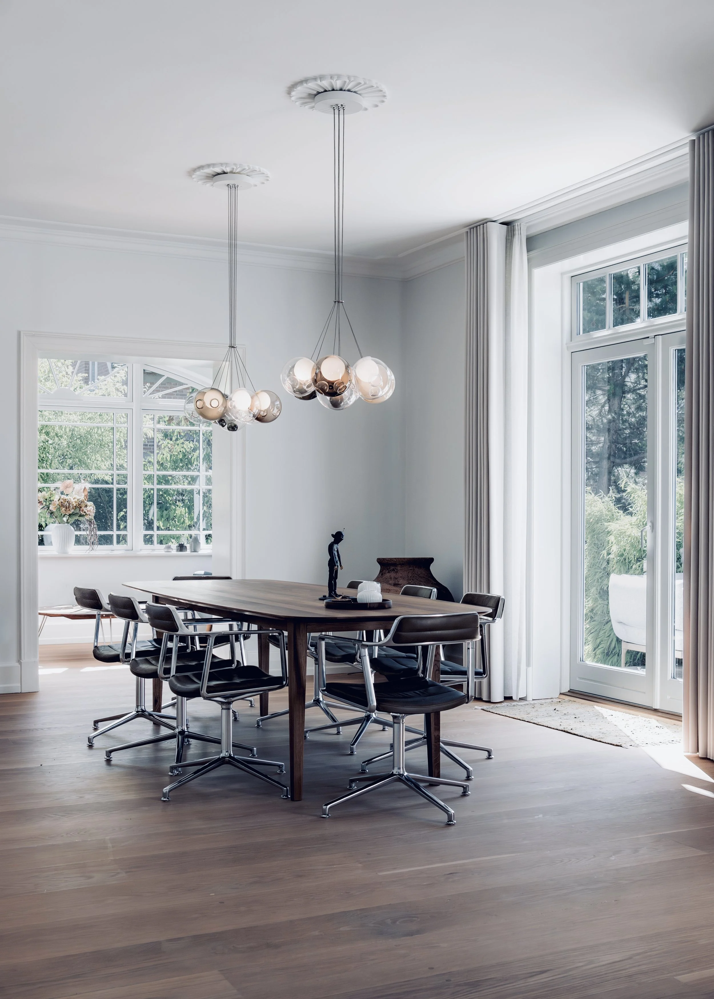 Modern dining room with wooden table, black chairs, large windows, and minimalist light fixtures.