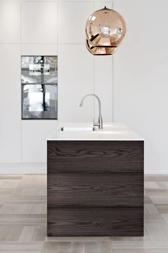 Modern kitchen with white cabinets, a dark wood island with a white countertop, a stainless steel faucet, a copper pendant light, and built-in oven units.