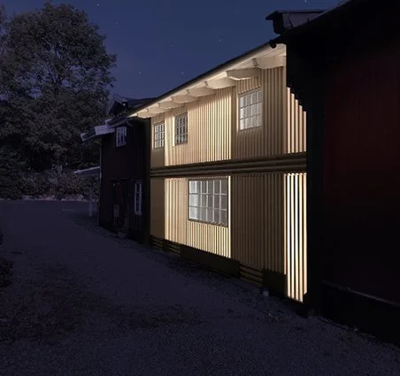 The exterior of a two-story house at night, illuminated by interior lights, with a background of trees and a dark sky.