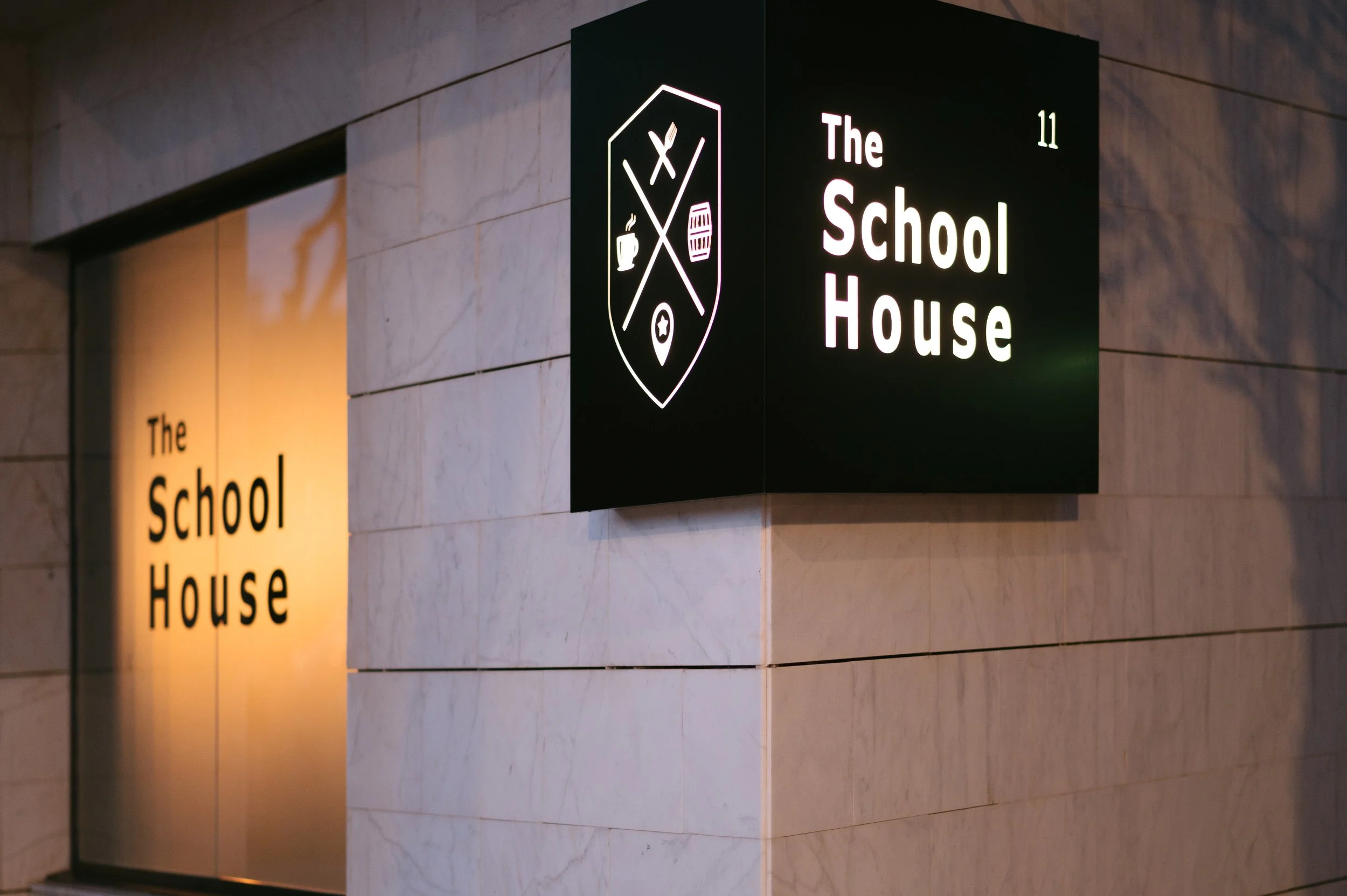 Sign for The School House with the building's name on a black background and illuminated text