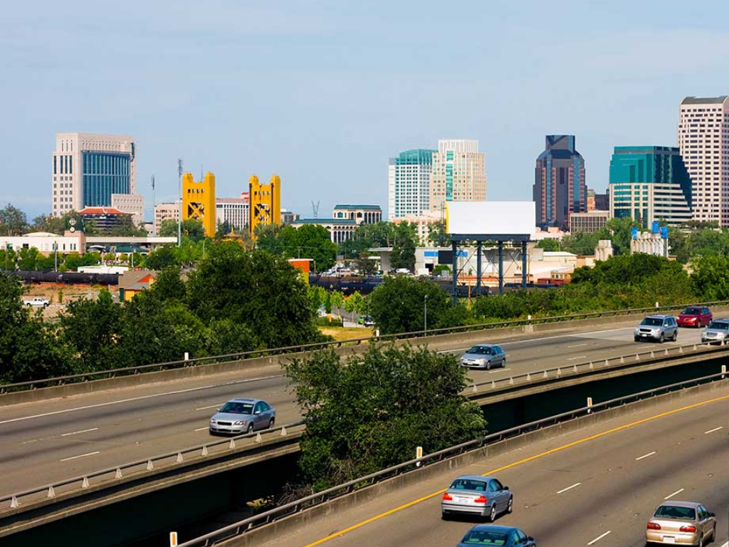City skyline with tall skyscrapers, highway with cars, and greenery in the foreground.