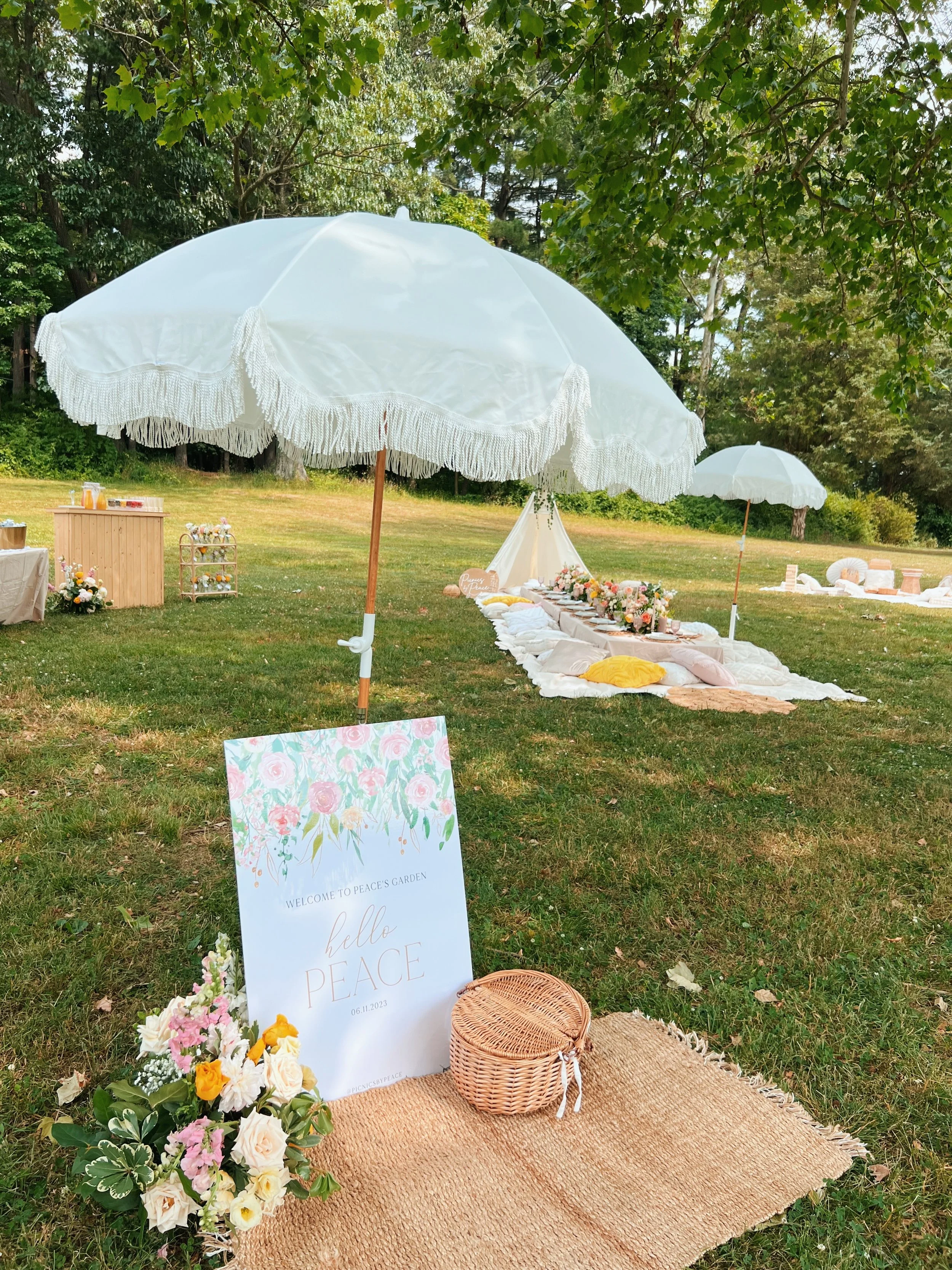 Large welcome sign displayed on an easel next to a wooden barrel outdoors near assorted pillows from Picnics By Peace