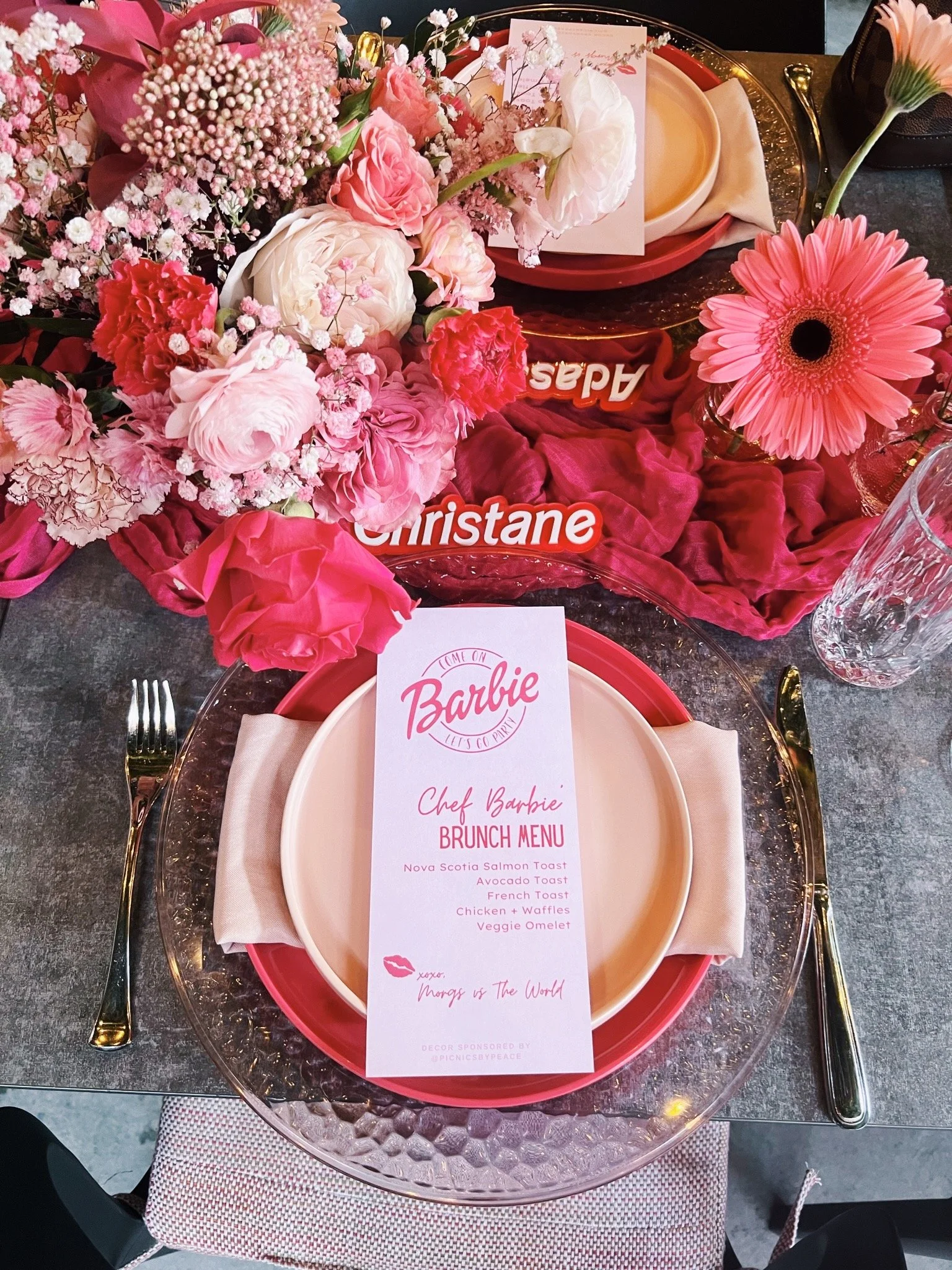 Customized menu cards on a small picnic table of assorted foods and drinks with a floral arrangement centerpiece designed by Picnics By Peace