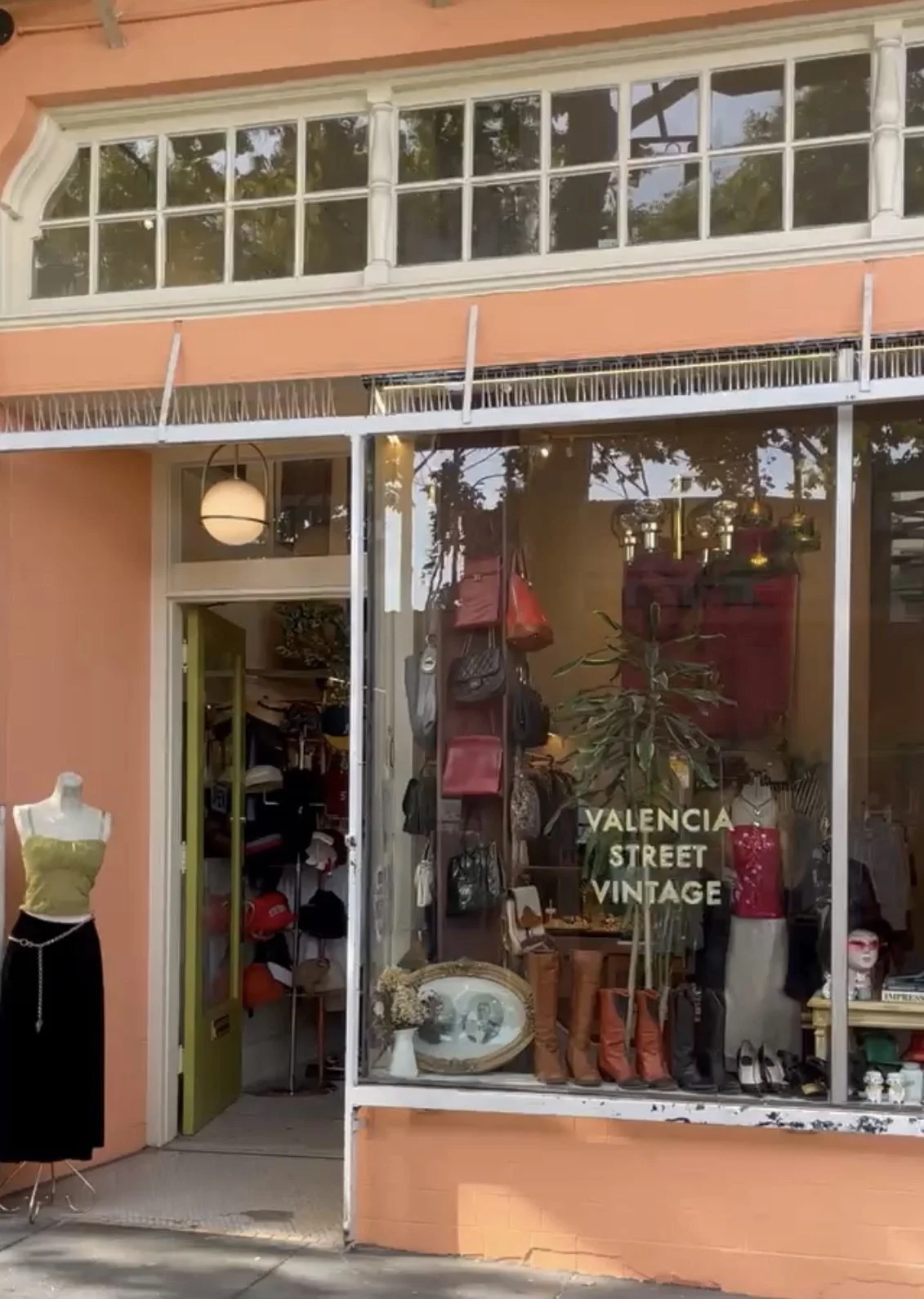 Vintage clothing and accessories store named Valencia Street Vintage with display window featuring bags, shoes, and decor, and an external mannequin wearing a gold top and black skirt.