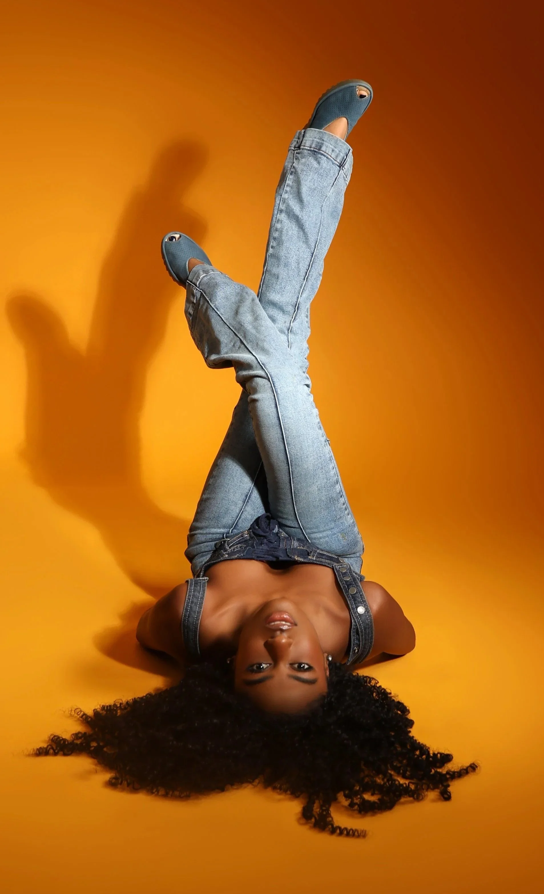 Canadian model and actress, Amanda Whyte styled in only denim posing in front of an orange backdrop.