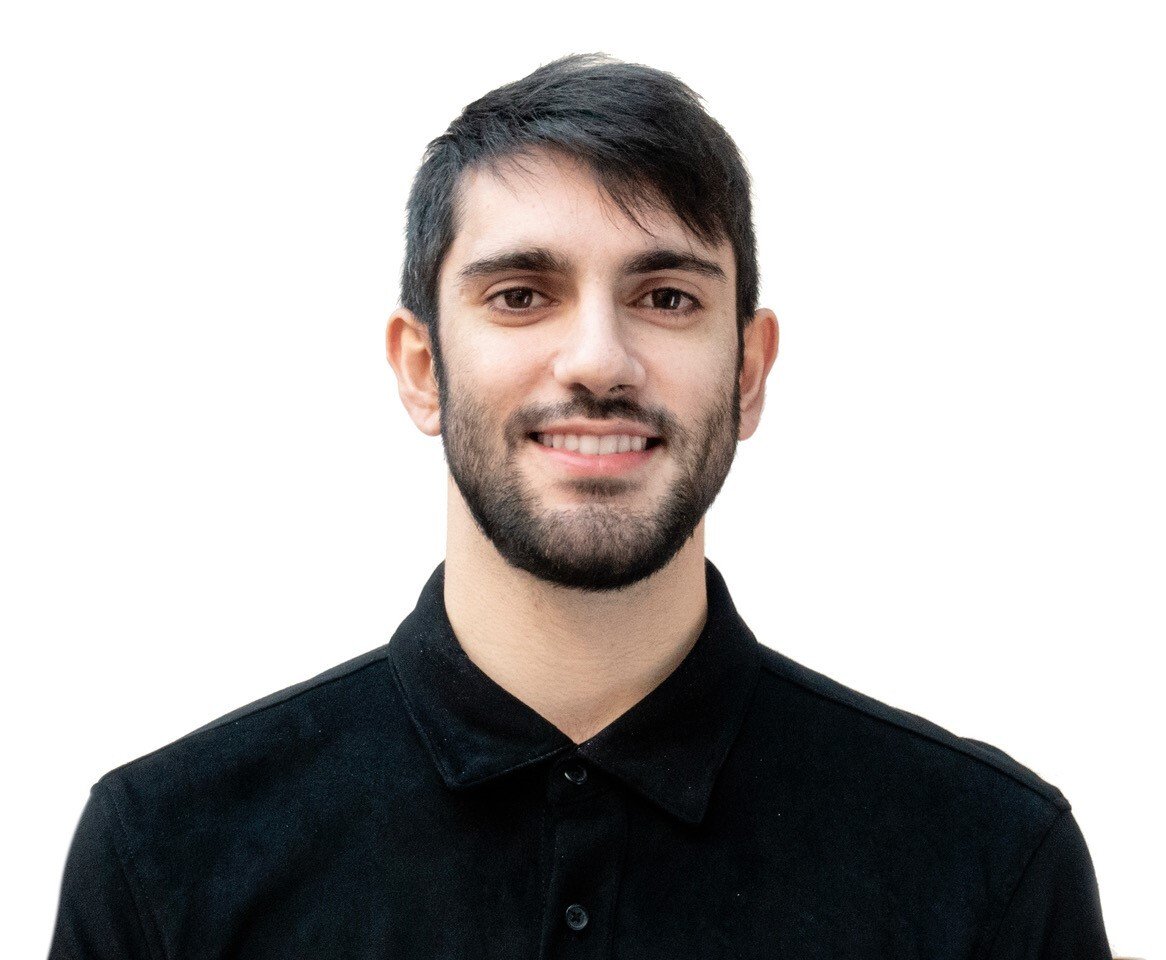 A portrait of a man with a beard and wearing a black shirt standing infront of a white background. 