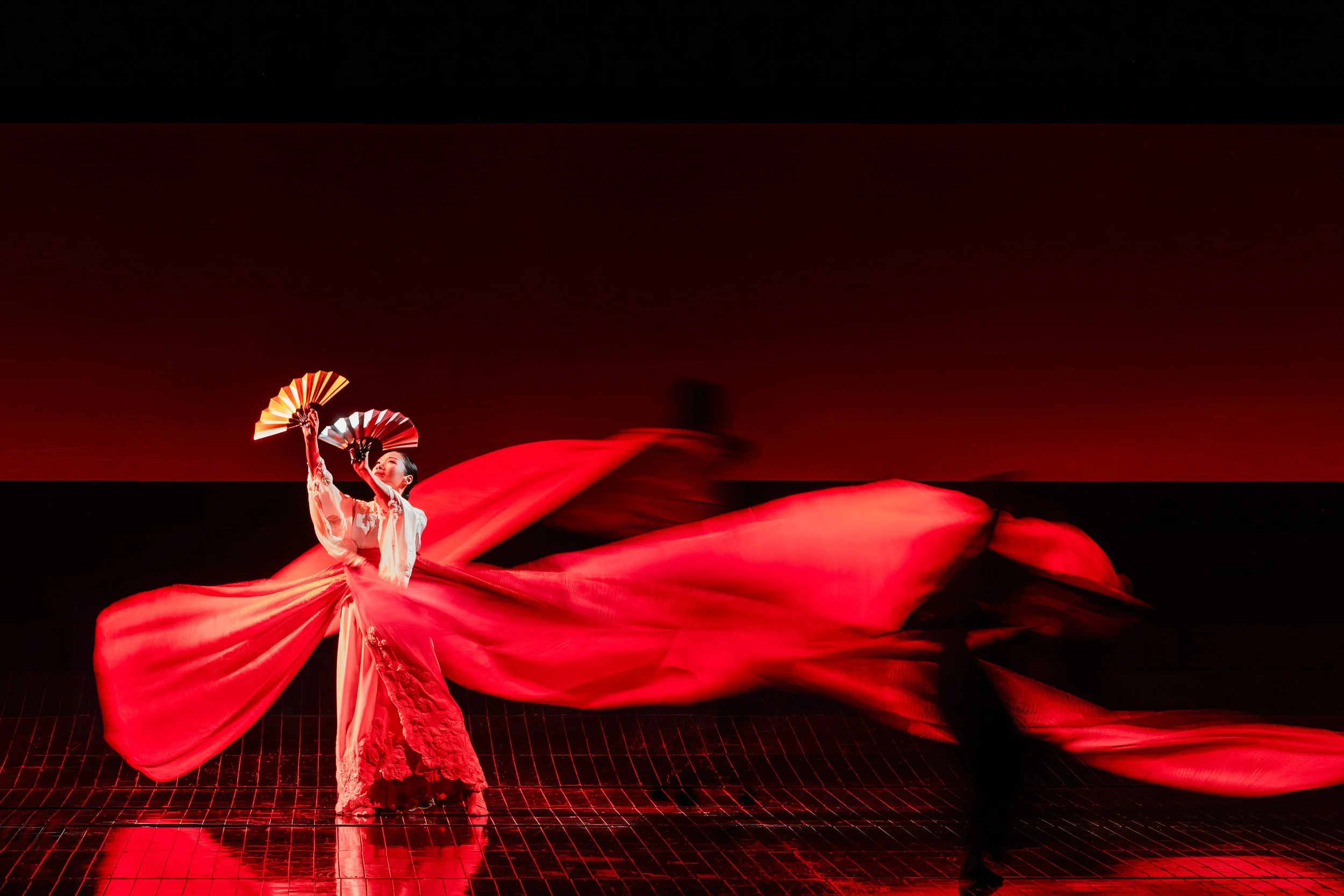 A dancer with two fans performs in a whirl of red silk.