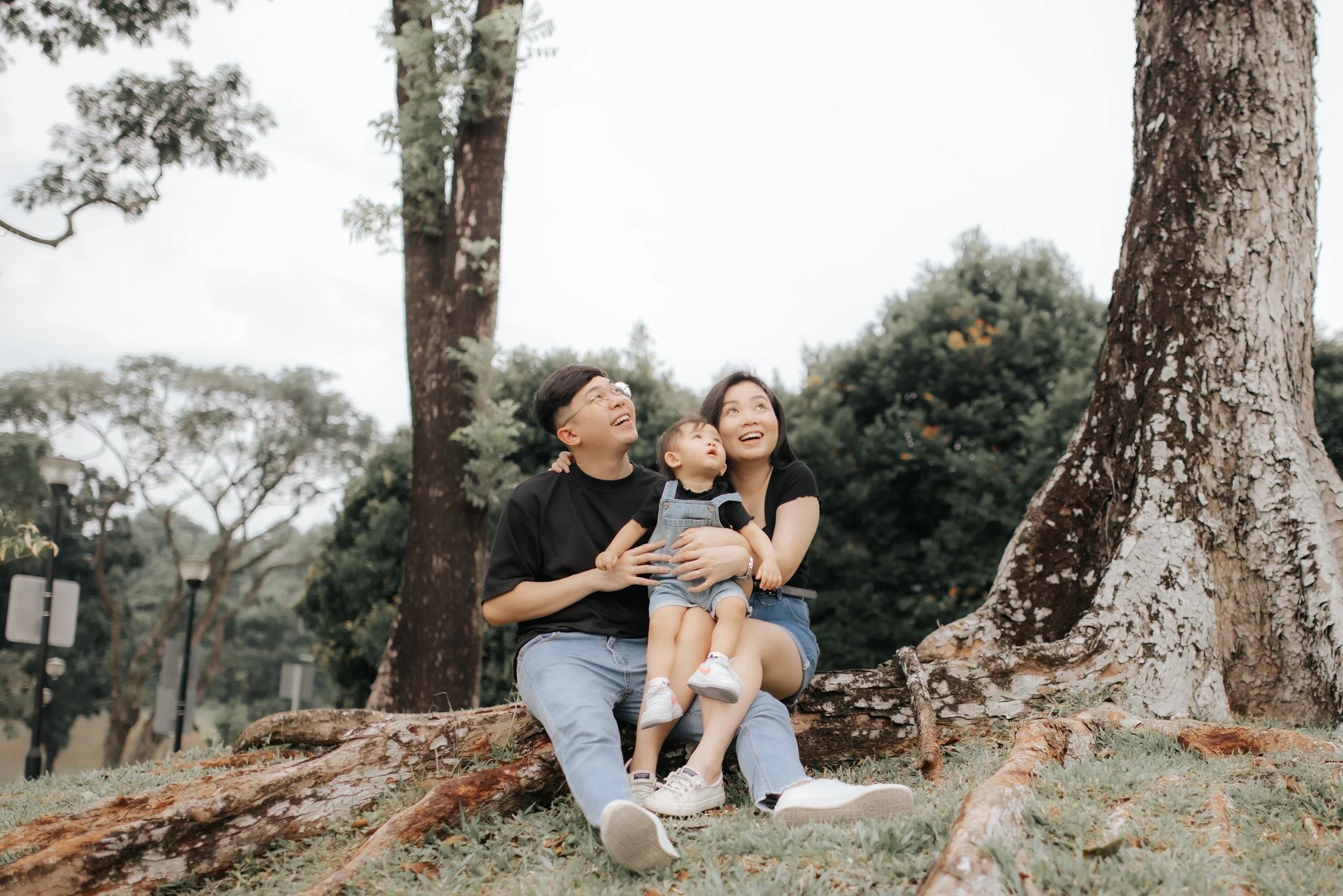 Light and airy family photo of a young family seated below a tree, captured in a soft outdoor setting in Singapore.