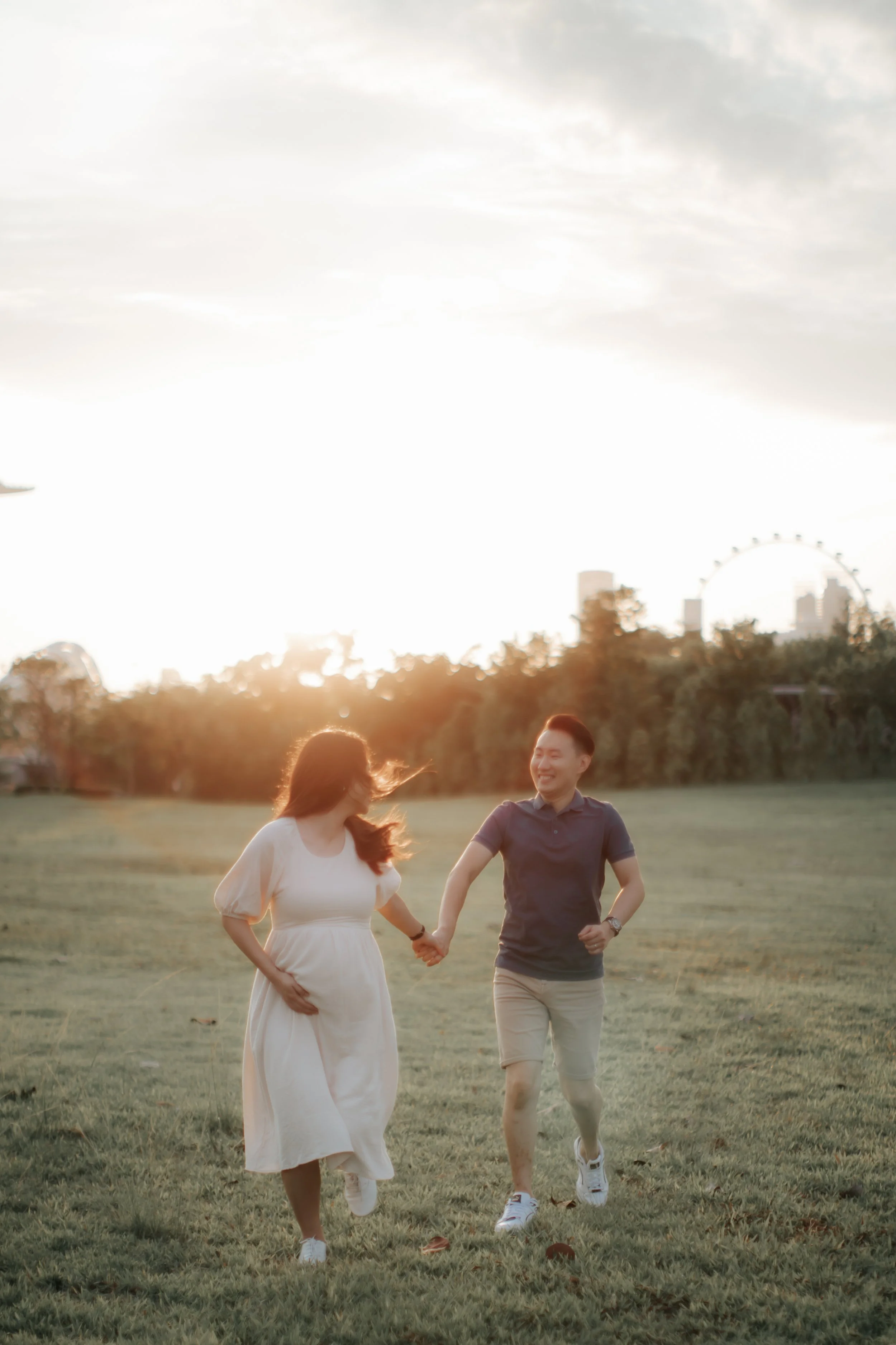 A couple during their maternity shoot taking a stroll at Gallop Extension in Singapore during golden hour as the sun sets behind them, captured by Breadandbutterworks in a soft and heartfelt style.