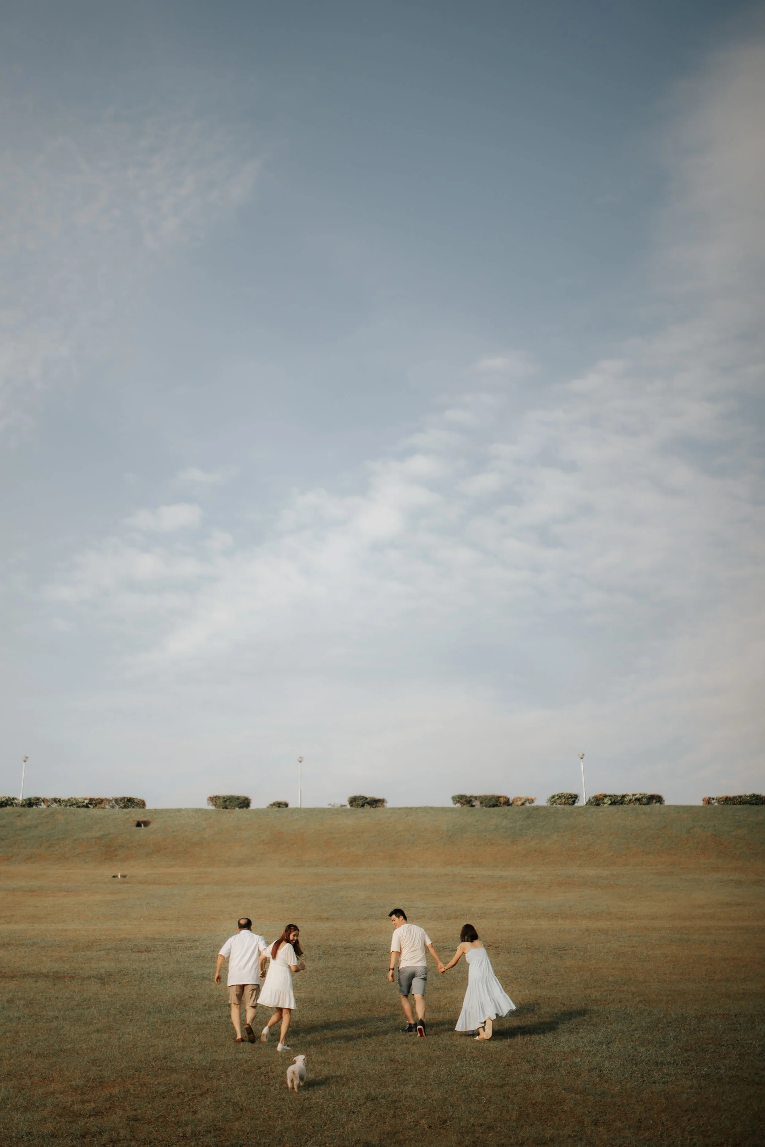 Light and airy family photoshoot in Singapore featuring a family strolling through a park outdoors with their pet dog, captured by Breadandbutterworks.