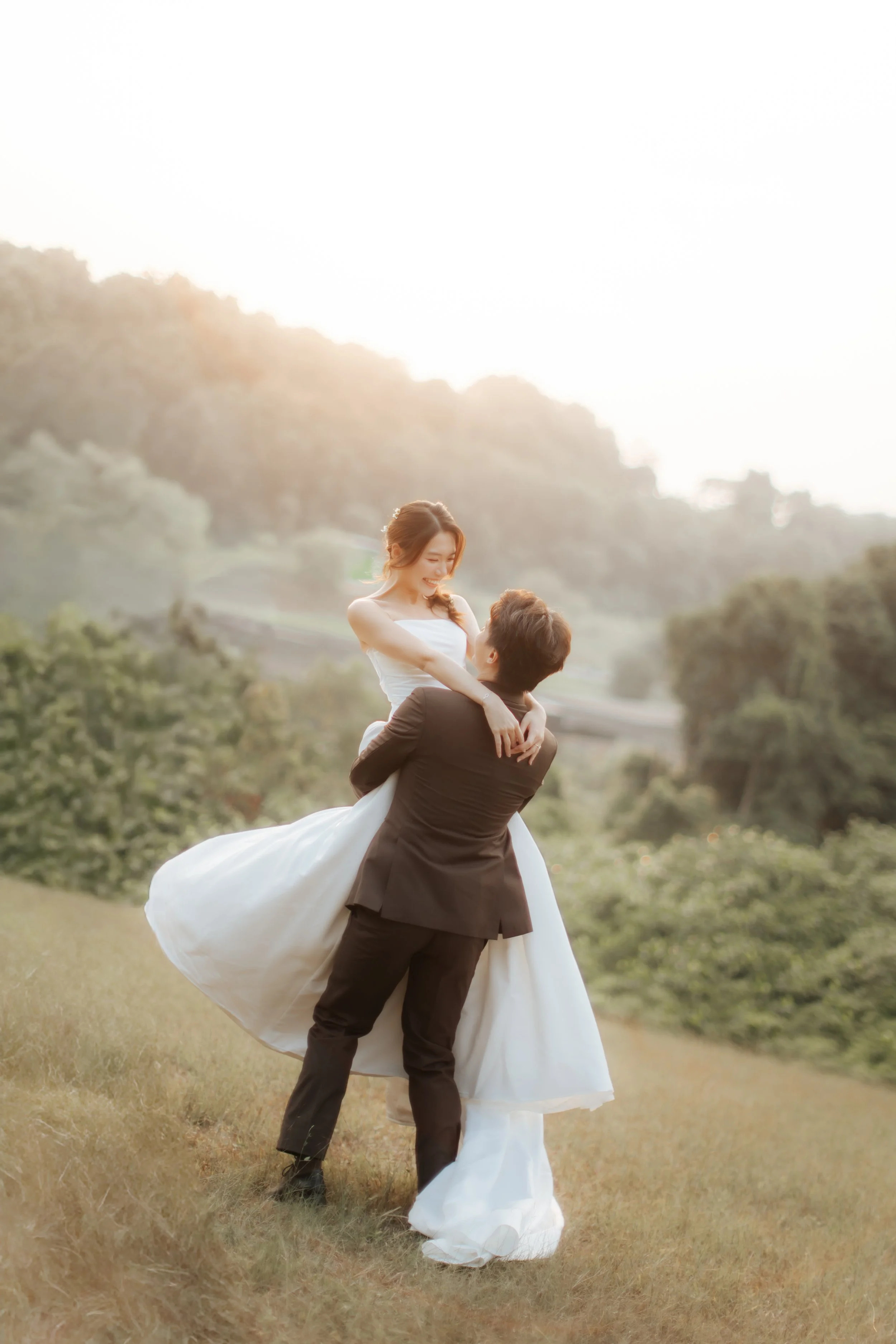 Romantic and dynamic pre-wedding photoshoot at Canterbury Hill. The groom is lifting up the bride and twirling her around as her gown trails behind gracefully. Captured in a light and airy style by Arielle from Breadandbutterworks.